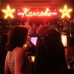 A couple enjoying a lively karaoke night in a dimly lit bar setting with neon lights.